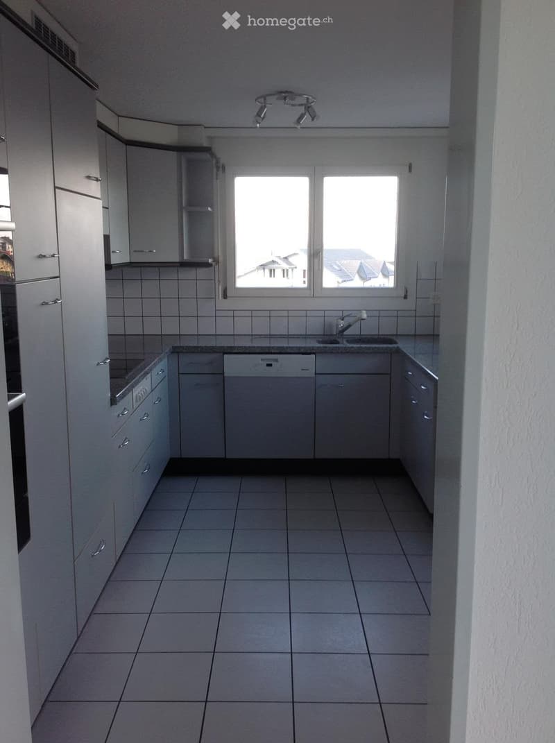 Modern kitchen with white cabinets, tiled floor, and a window overlooking a residential area.