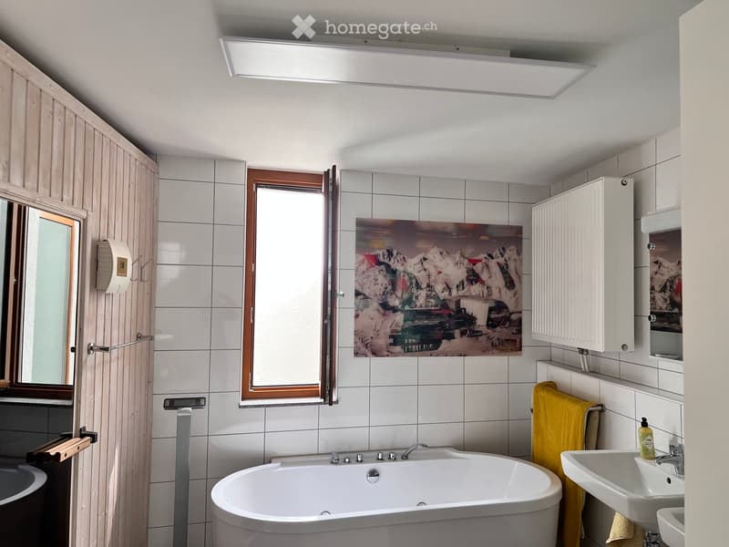 Modern bathroom with a bathtub, sink, mirror, and cabinet. Features a large window, a painting on the wall, and a yellow towel hanging on a rack.