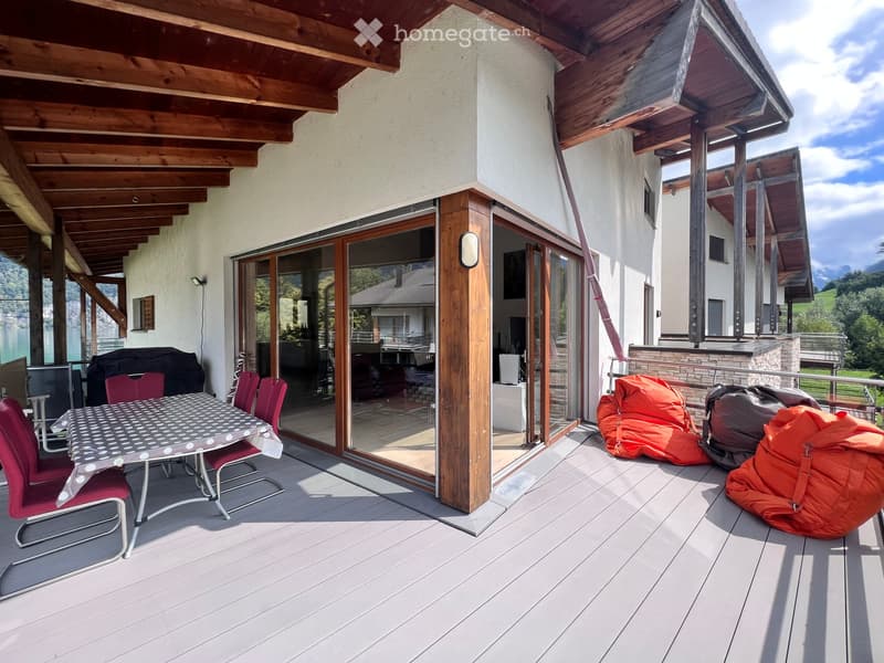 Balcony with wooden decking, large glass doors, outdoor table and chairs, red bean bags, scenic mountain view.