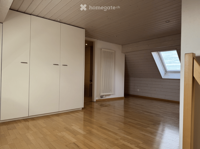 Empty room with wooden flooring, white walls, built-in white closet, radiator, and skylight window.