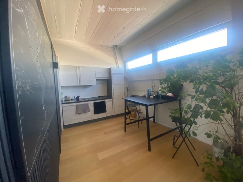 Modern kitchen with white cabinets, wooden flooring, a black dining table, and a potted plant near the window.