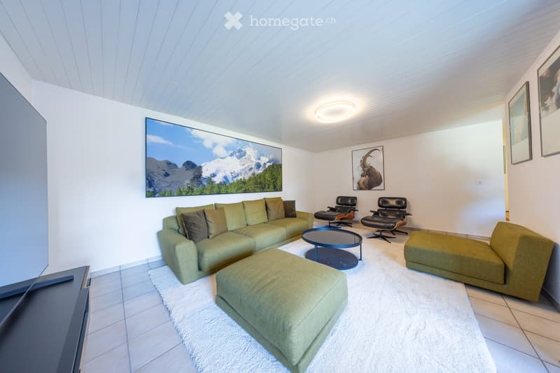Modern living room with a green sectional sofa, ottomans, a round coffee table, two leather chairs, and artwork on the walls.