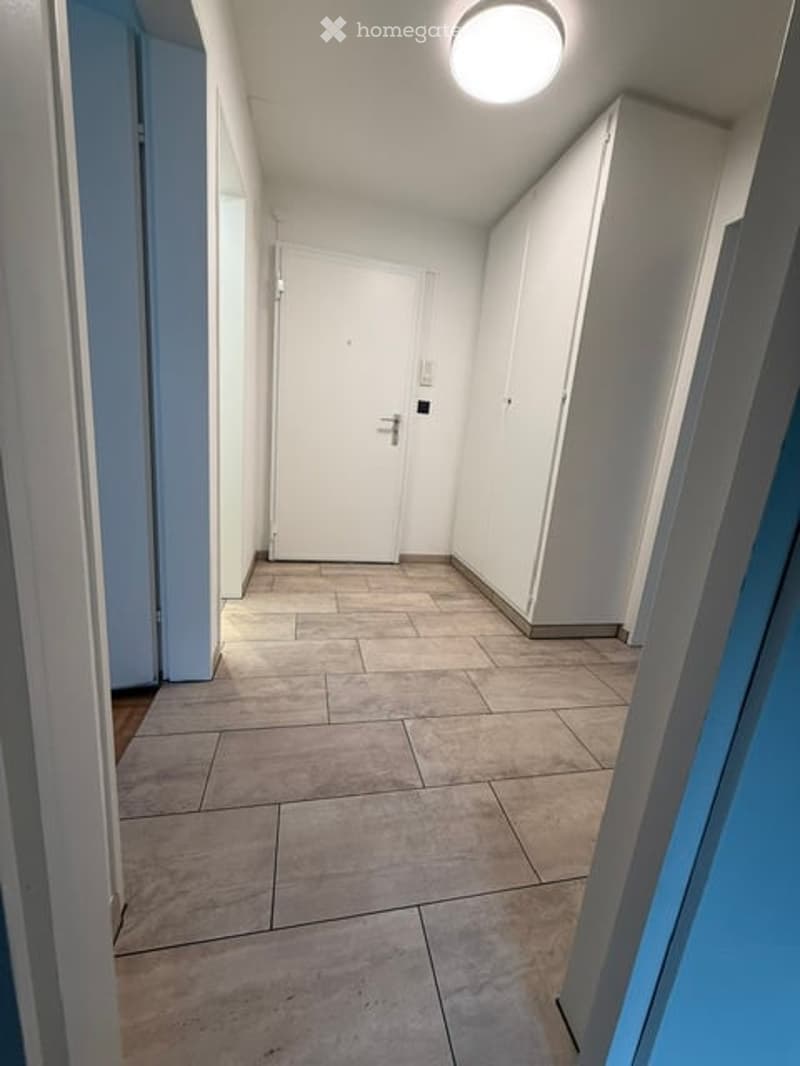 Empty hallway with tiled floor, white walls, and a closed door at the end.