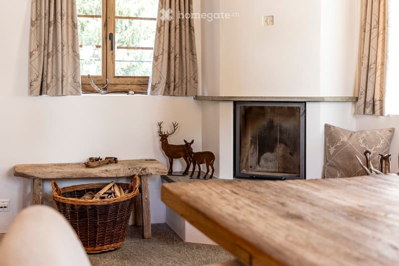 Cozy living room with a fireplace, wooden bench, wicker basket with firewood, deer figurines, cushion, and wooden table.