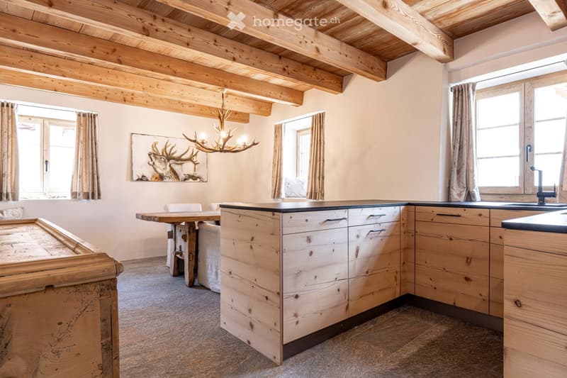Cozy kitchen with wooden cabinets, island, sink, chandelier, and large windows with curtains.