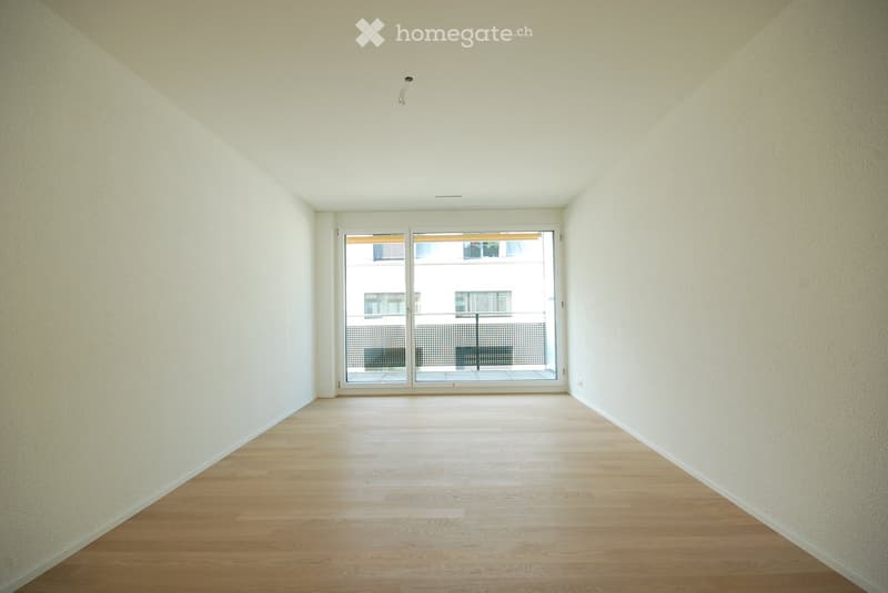 Empty room with wooden flooring, white walls, and a large sliding glass door leading to a balcony.