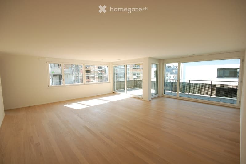 Empty room with wooden flooring and large windows, including sliding glass doors leading to a balcony.