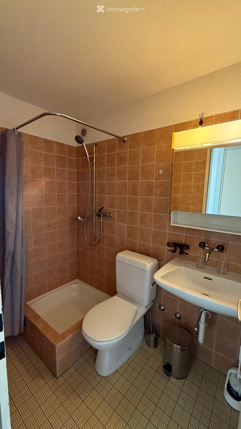 Bathroom with beige tiles, a toilet, a sink, a bathtub, a shower, and a mirror above the sink.
