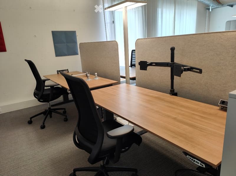 Modern office space with wooden desks, ergonomic chairs, and privacy screens.