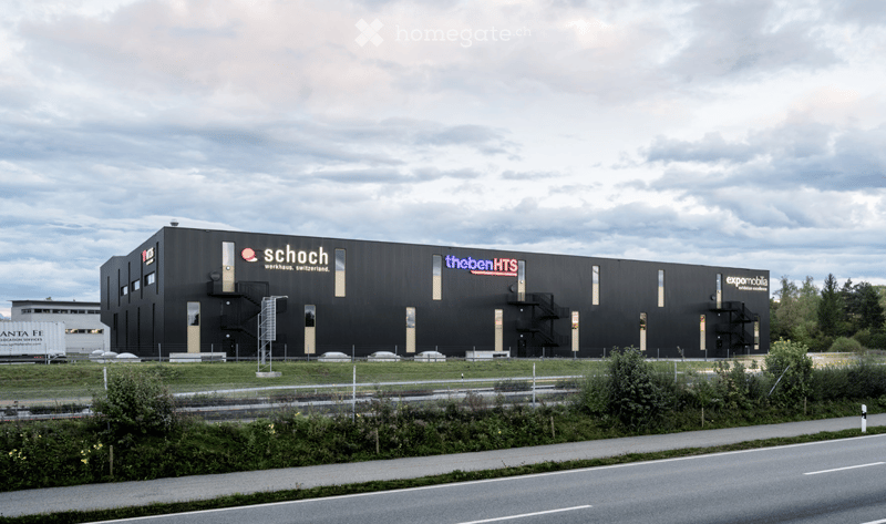 Modern industrial-style building with a black facade, large windows, and signage for 'Schoch' and 'thebenHTS'.