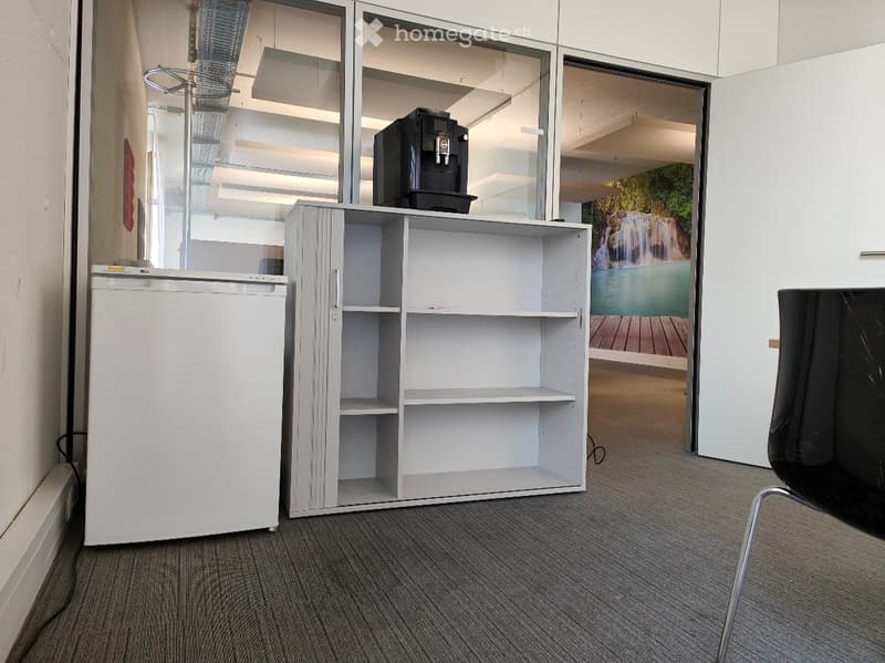 Break room with a small refrigerator, coffee machine on a shelf, and a black chair near a glass wall with a scenic view.
