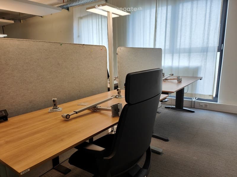 Office space with a wooden table, ergonomic chair, and screen partitions for privacy.