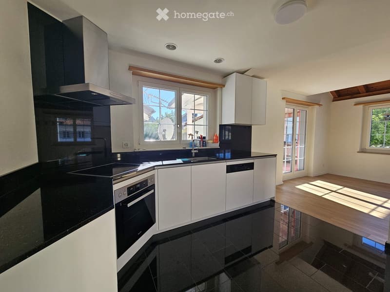 Modern kitchen with white cabinets, black countertops, stainless steel appliances, and a large window overlooking the street.