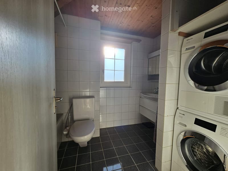 Bathroom with white tiled walls, black tiled floor, toilet, sink, and stacked washing machine and dryer unit.