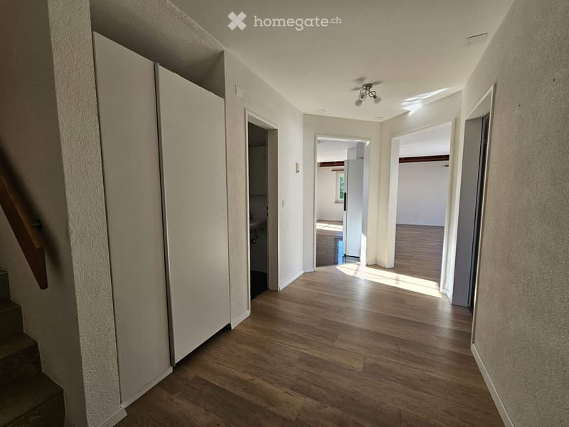 Empty hallway with wooden flooring, white walls, and several open doors leading to other rooms.