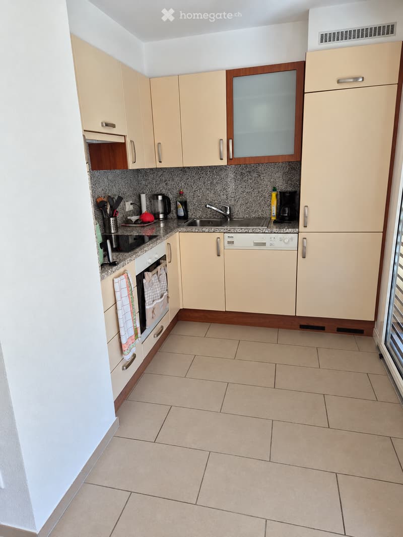 Modern kitchen with light-colored cabinets, granite countertops, and tiled flooring. Features an oven, dishwasher, sink, and various kitchen utensils.