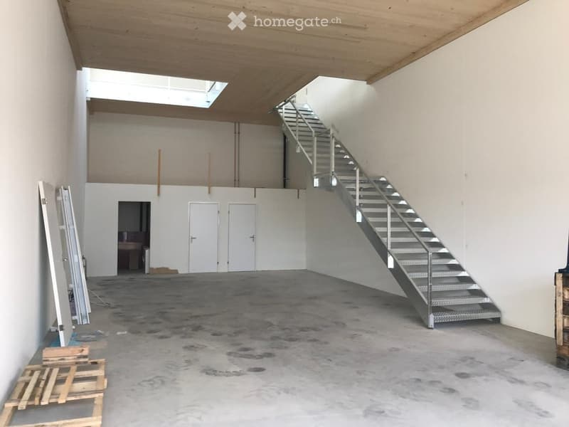 Empty room with concrete floor, white walls, metal staircase leading to an upper level, and a small window at the top.