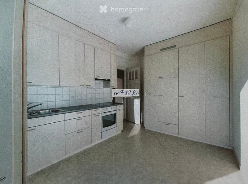 Empty kitchen with white cabinets, a sink, and an oven. The space is clean and unfurnished.