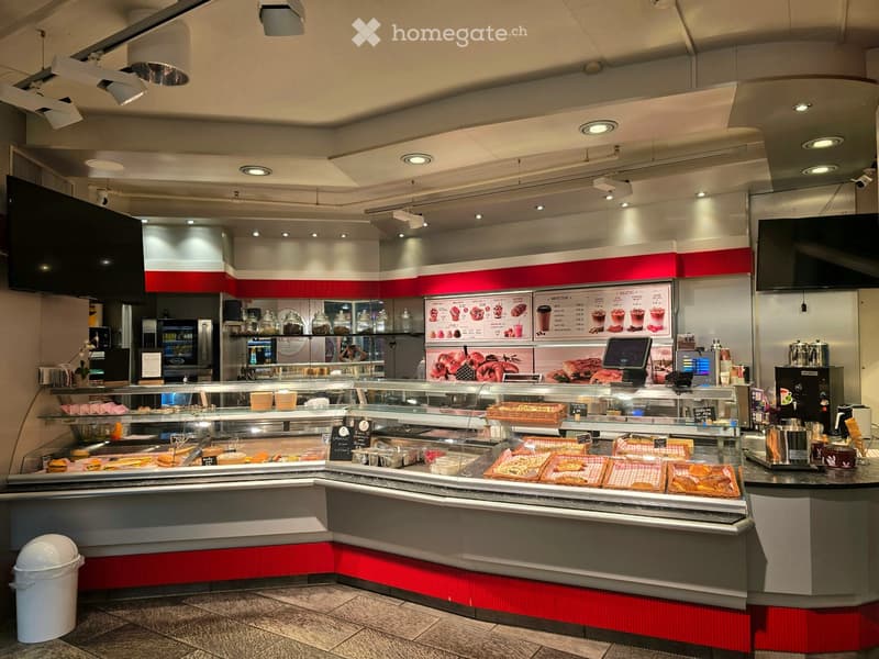 Modern food service area with display case, menu board, refrigerator, and various kitchen equipment.