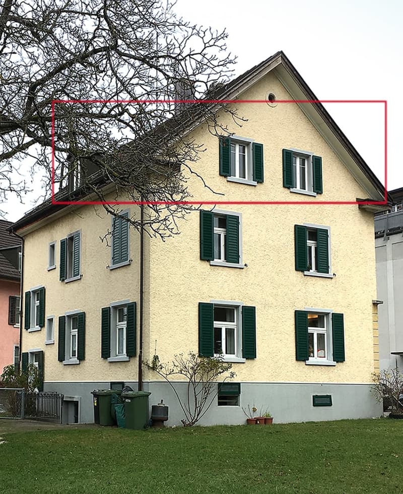 Two-story house with yellow facade, green shutters, multiple windows, and a small garden area with trash bins.