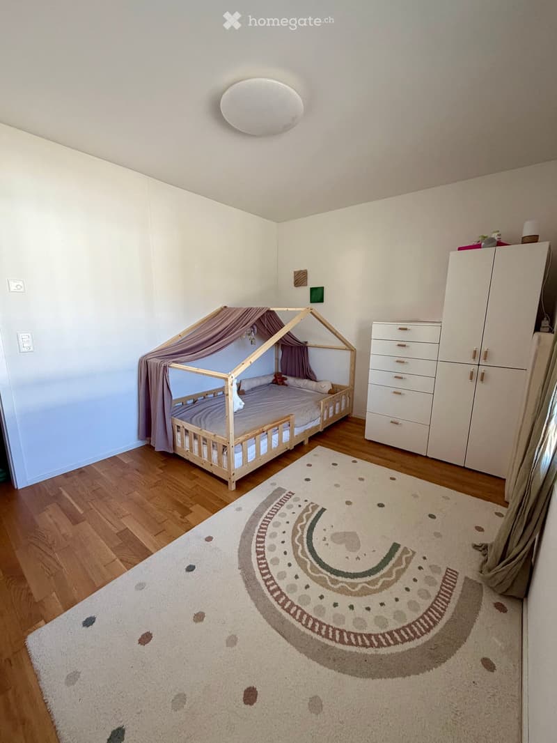 Cozy children's bedroom with a wooden bed, white wardrobe, and a large patterned rug on the floor.
