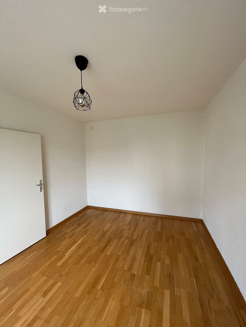 Empty room with wooden flooring, white walls, and a single hanging light fixture.