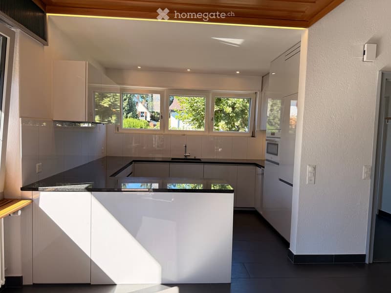 Modern kitchen with white cabinets, black countertop, and large windows letting in natural light.
