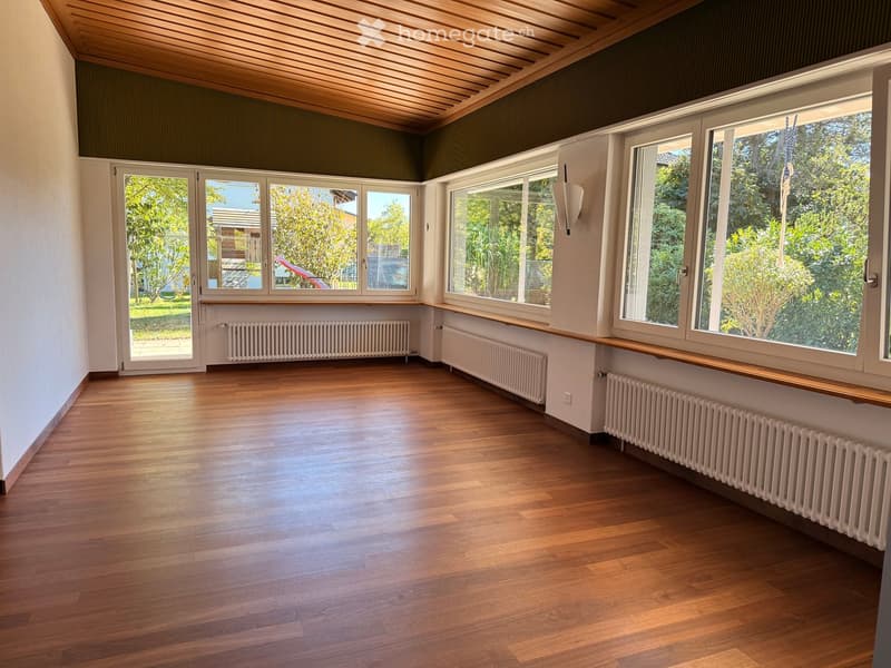 Empty room with wooden flooring, large windows, radiators, and a slanted wooden ceiling.