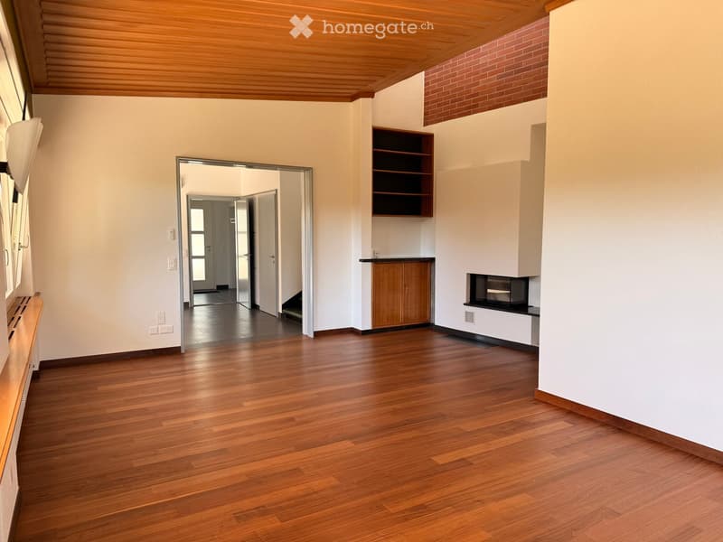 Empty room with wooden flooring, white walls, and a built-in shelving unit. The room features a fireplace and a sliding glass door leading to another space.