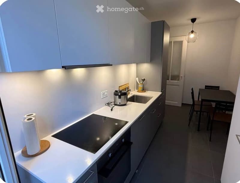 Modern kitchen with white cabinets, induction cooktop, oven, sink, and a small dining area with a table and chairs.