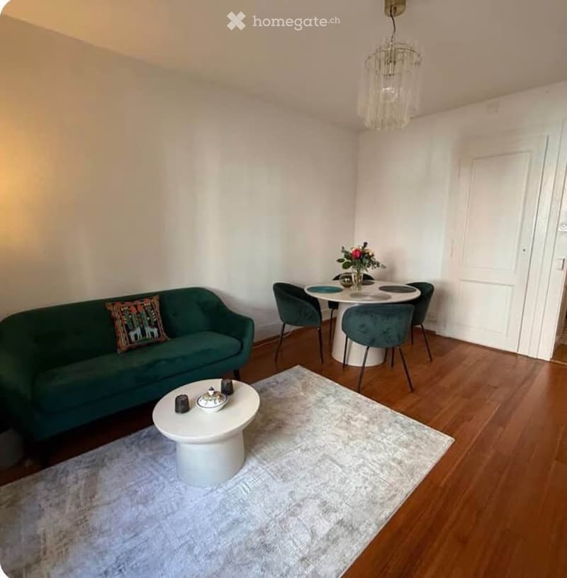 A modern living and dining area with a green sofa, white coffee table, dining table with chairs, and a chandelier.