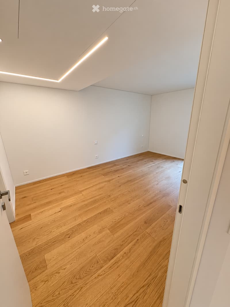 Empty room with light wooden flooring and white walls, featuring recessed lighting and electrical outlets.