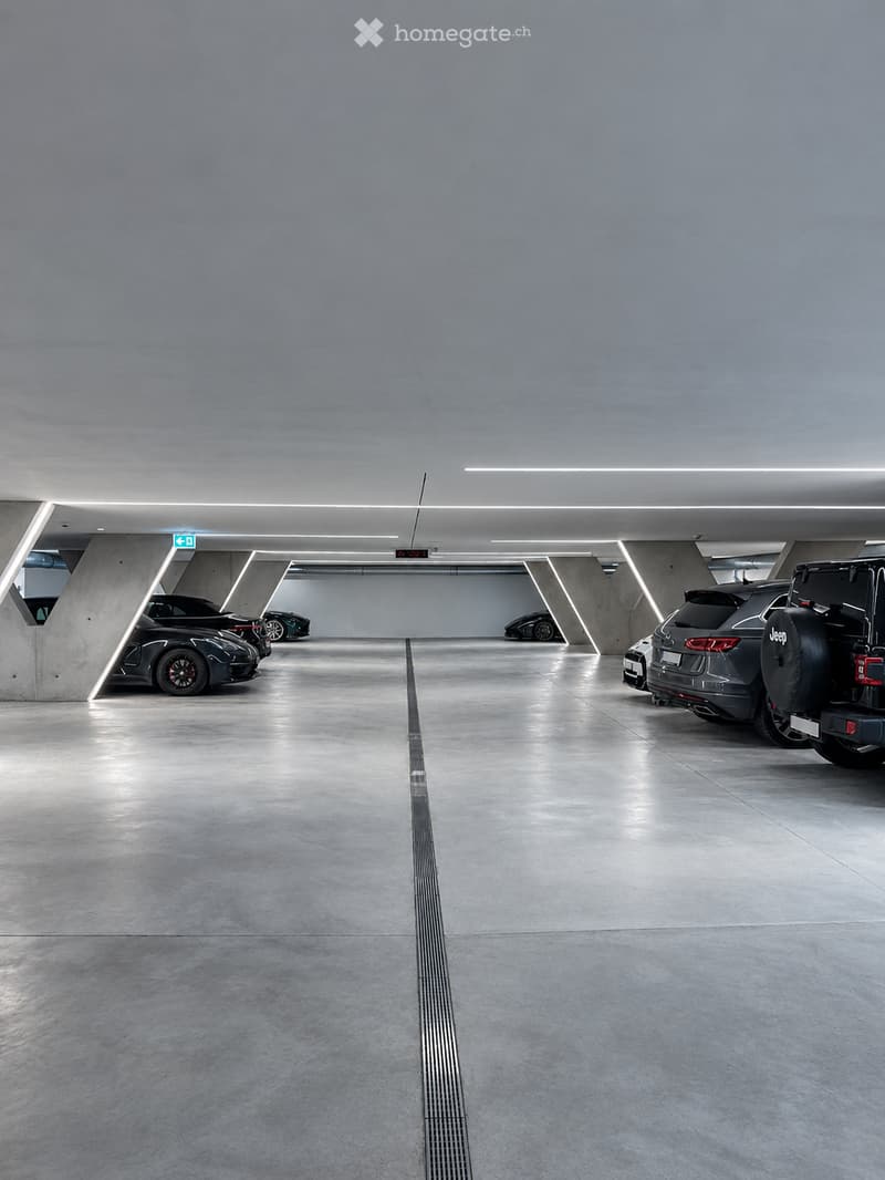 Modern underground parking area with several parked cars, clean concrete floors, and sleek lighting fixtures.