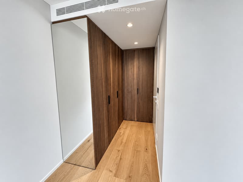 Modern hallway with light wooden flooring, white walls, and built-in wooden closet doors.