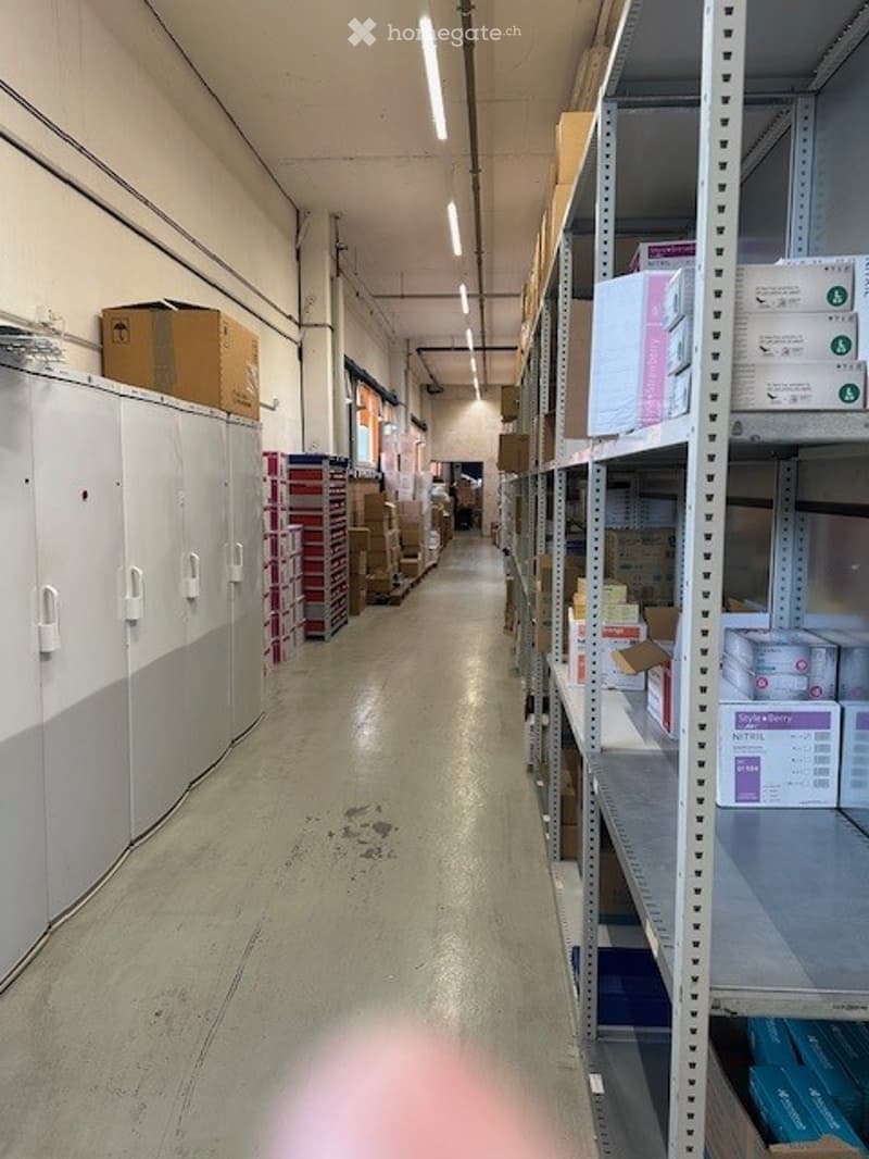 Warehouse, storage boxes on shelves, brown cardboard boxes on the floor, white cabinets, white ceiling lights, grey floor.