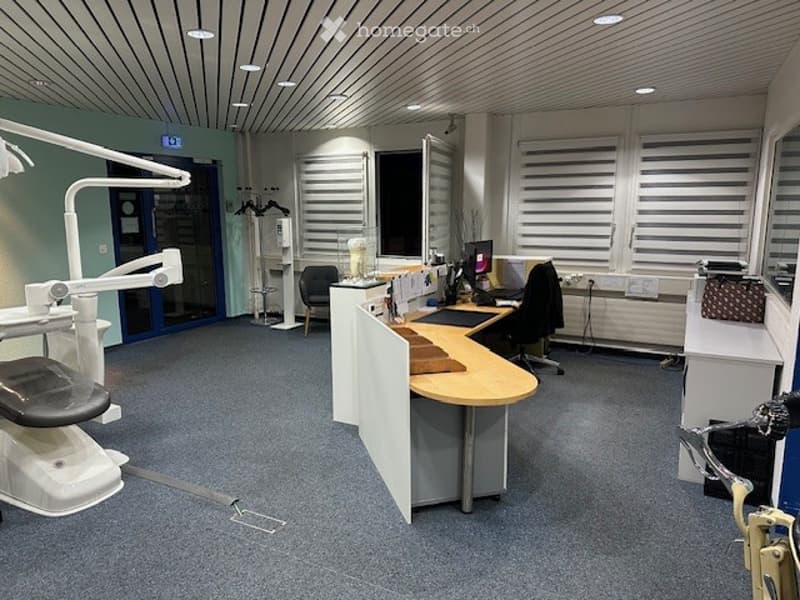 empty room, white walls, ceiling lights, glass door, blue door, gray floor, white cabinets, chair, desk, computer, monitor
