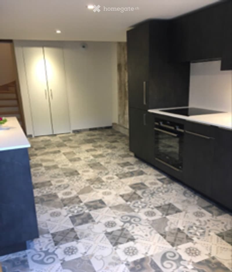 Modern kitchen with black cabinets, white countertops, and a decorative patterned tile floor. Features an oven and stove, with a large white pantry door visible in the background.