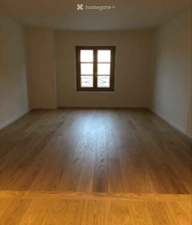 Empty room with wooden flooring and a single window allowing natural light to enter.