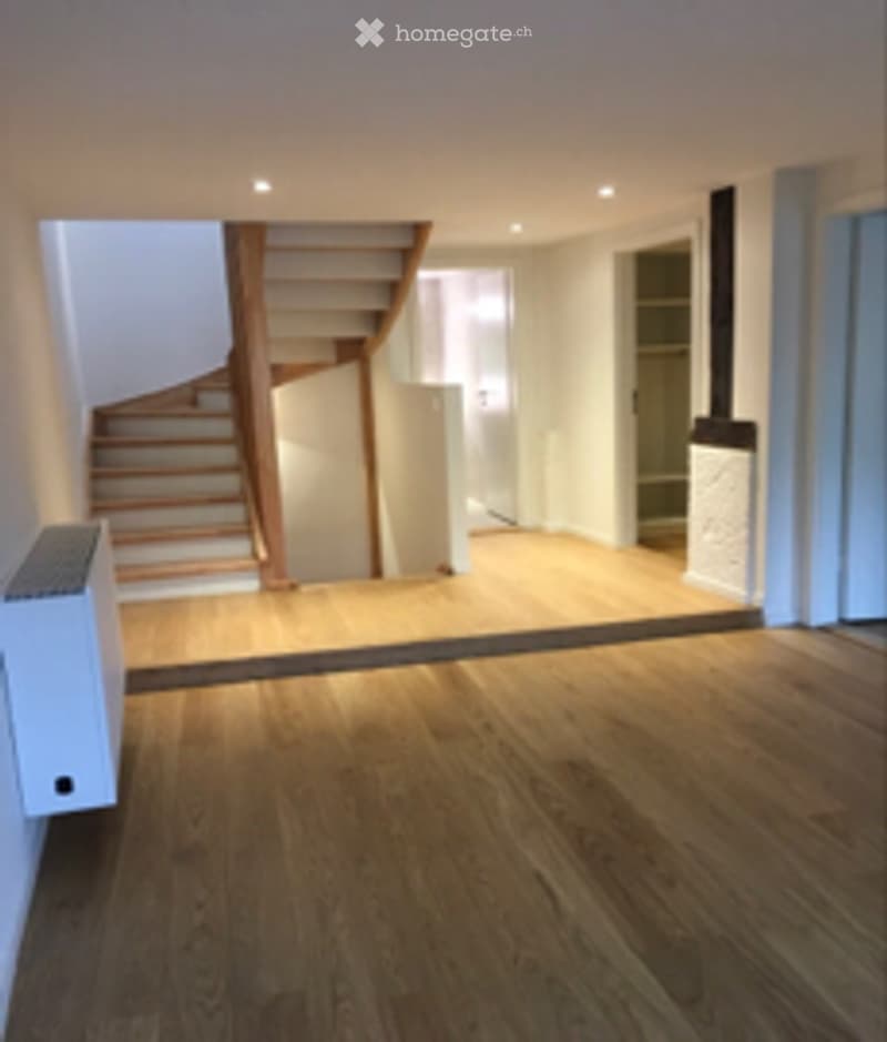Empty room with wooden flooring, a staircase leading upwards, and recessed lighting. No furniture or equipment is present.