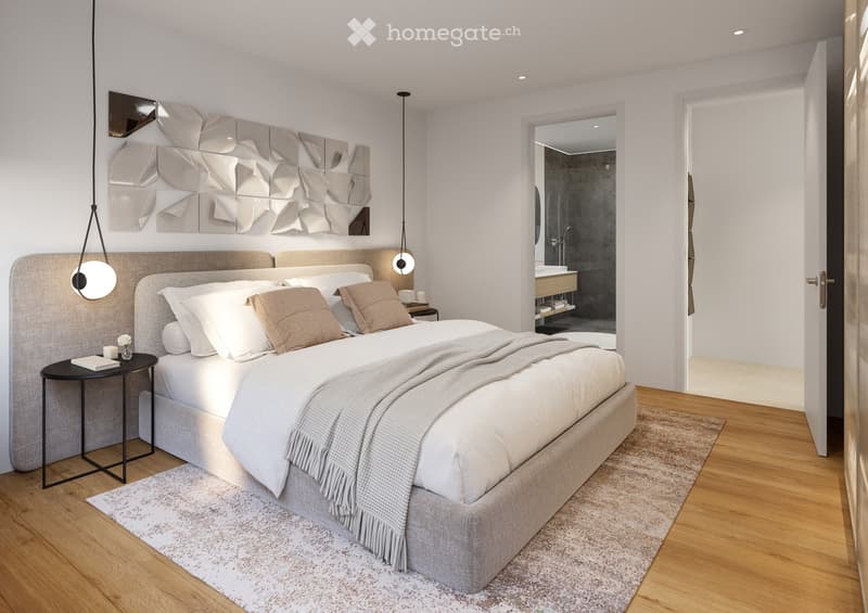 Modern bedroom with a large bed, nightstand, pendant lights, and a decorative wall mirror. The room features wooden flooring and a small adjacent bathroom visible through an open doorway.