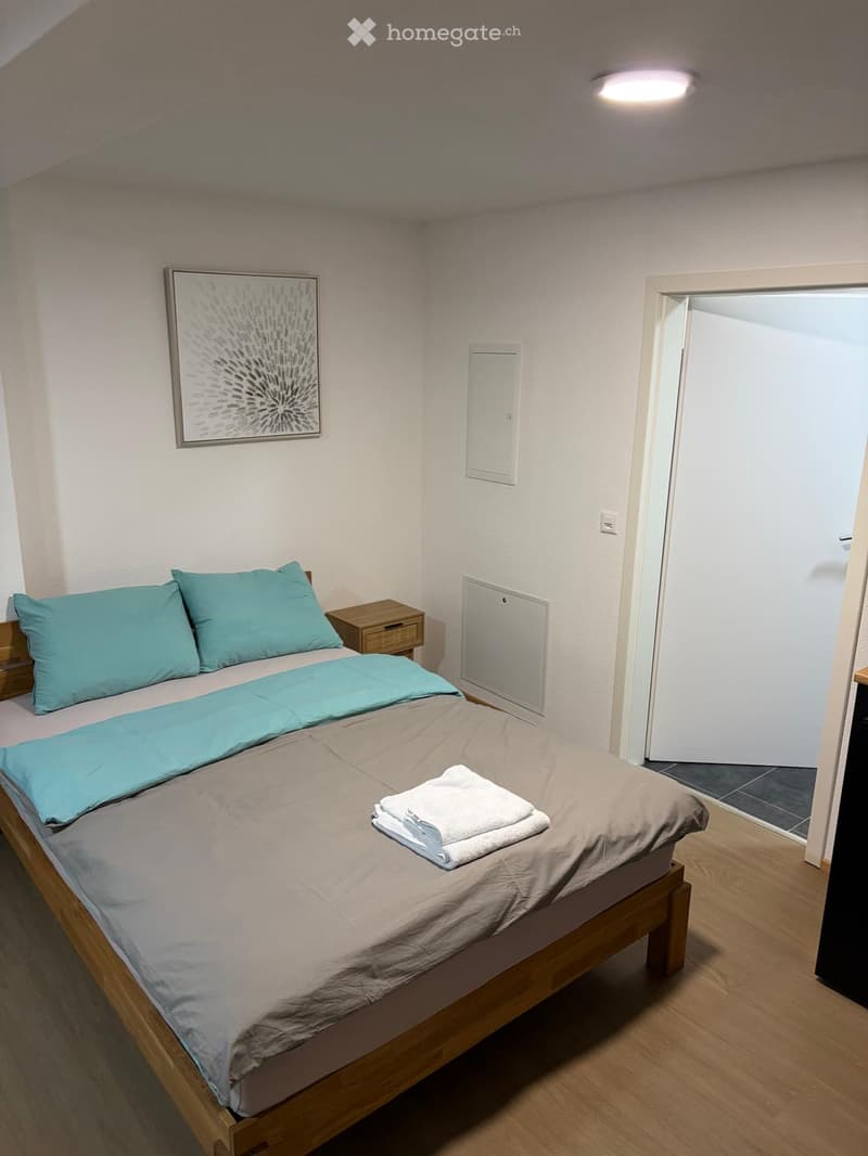 Cozy bedroom with a wooden bed, light blue bedding, a nightstand, and a framed picture on the wall. A towel is placed on the bed.