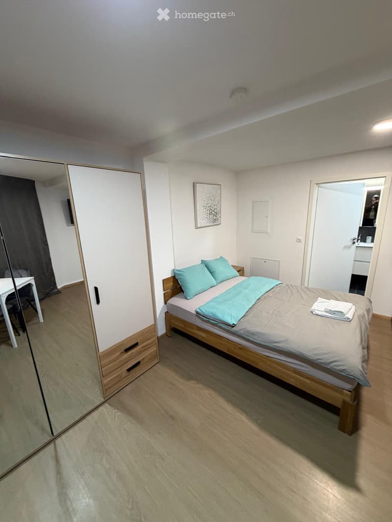 Cozy bedroom with a single bed, nightstand, mirror, wardrobe, and a small table with a chair.