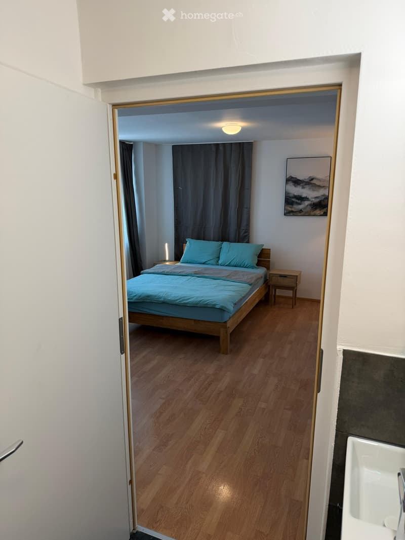 Cozy bedroom with wooden flooring, a double bed with blue bedding, a nightstand, and a painting on the wall.