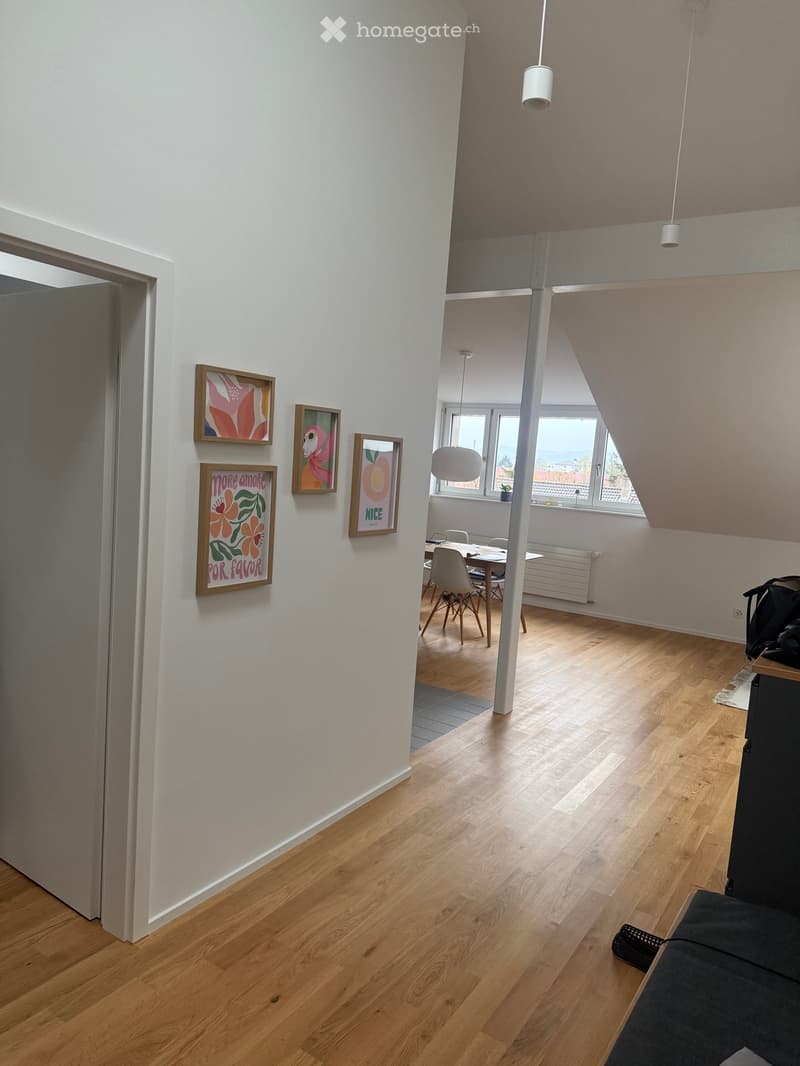 Open-plan living and dining area with light wooden flooring, white walls, and modern decor including framed art and a small dining set.