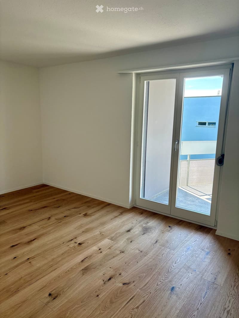 Empty room with light wooden flooring and white walls, featuring a large sliding glass door leading to a balcony area.