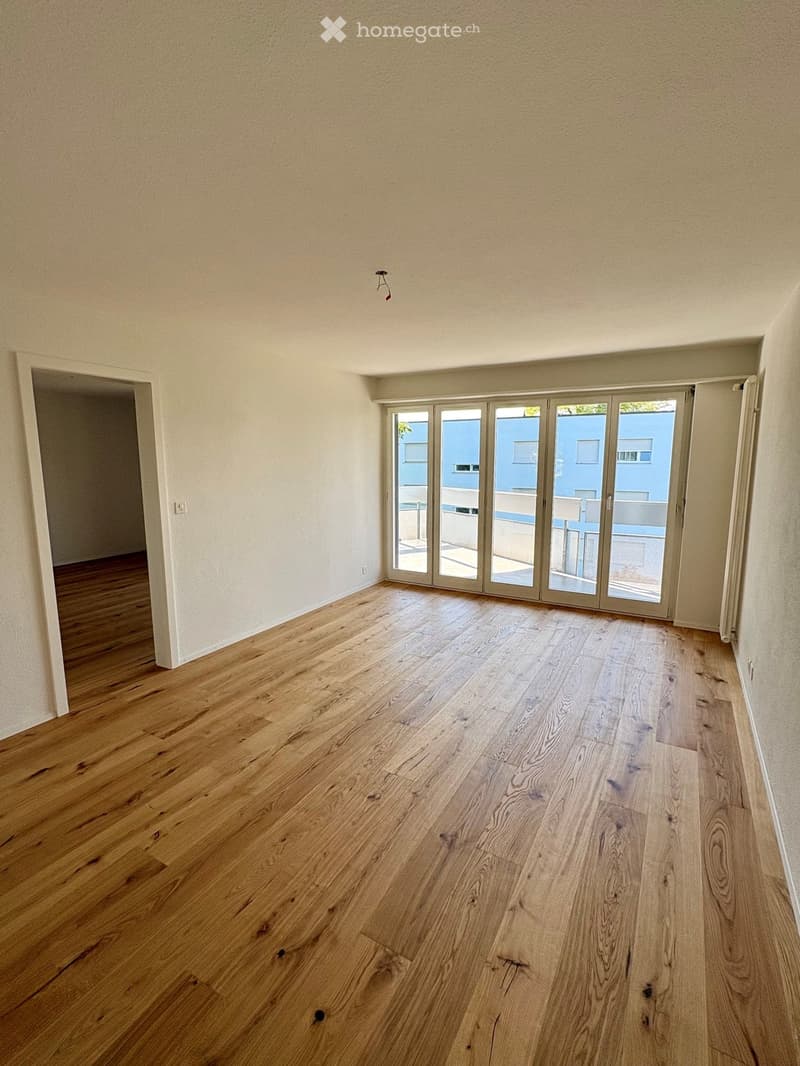 Empty room with wooden flooring, large sliding glass doors leading to a balcony, and neutral-colored walls.