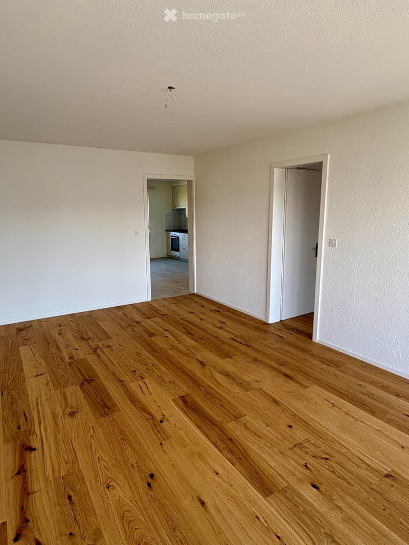 Empty room with wooden flooring and white walls, featuring two open doors leading to other rooms.