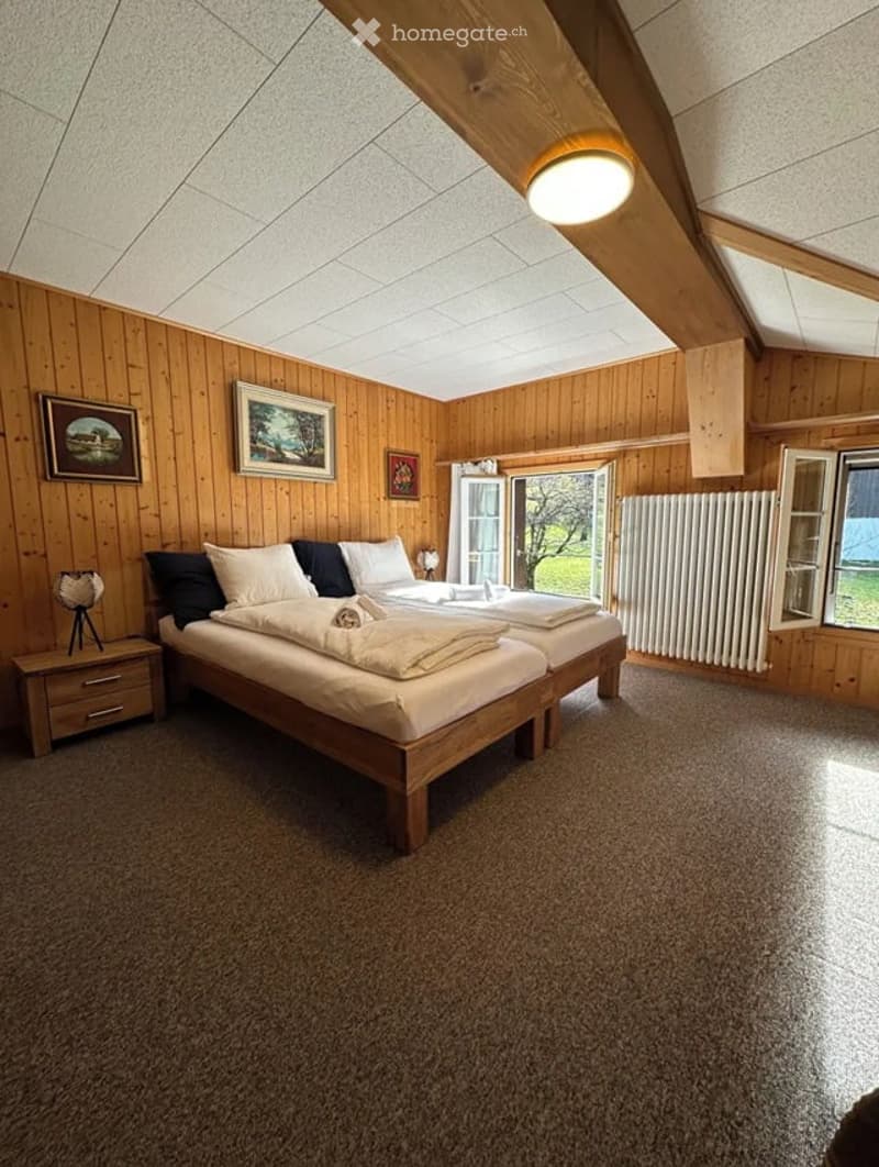Cozy bedroom with wooden walls, two single beds, nightstand, lamp, radiator, and picture frames on the wall.
