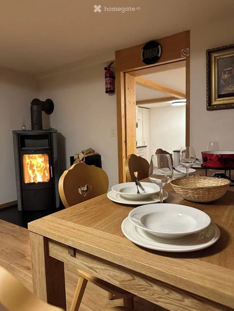 Cozy dining area with a wooden table, chairs, fireplace, and wine glasses on the table.