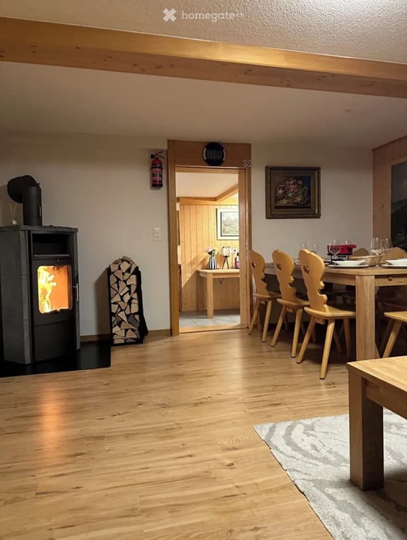 Cozy living and dining area with wooden flooring, a fireplace, a dining table with chairs, and a small kitchen area visible through an open doorway.